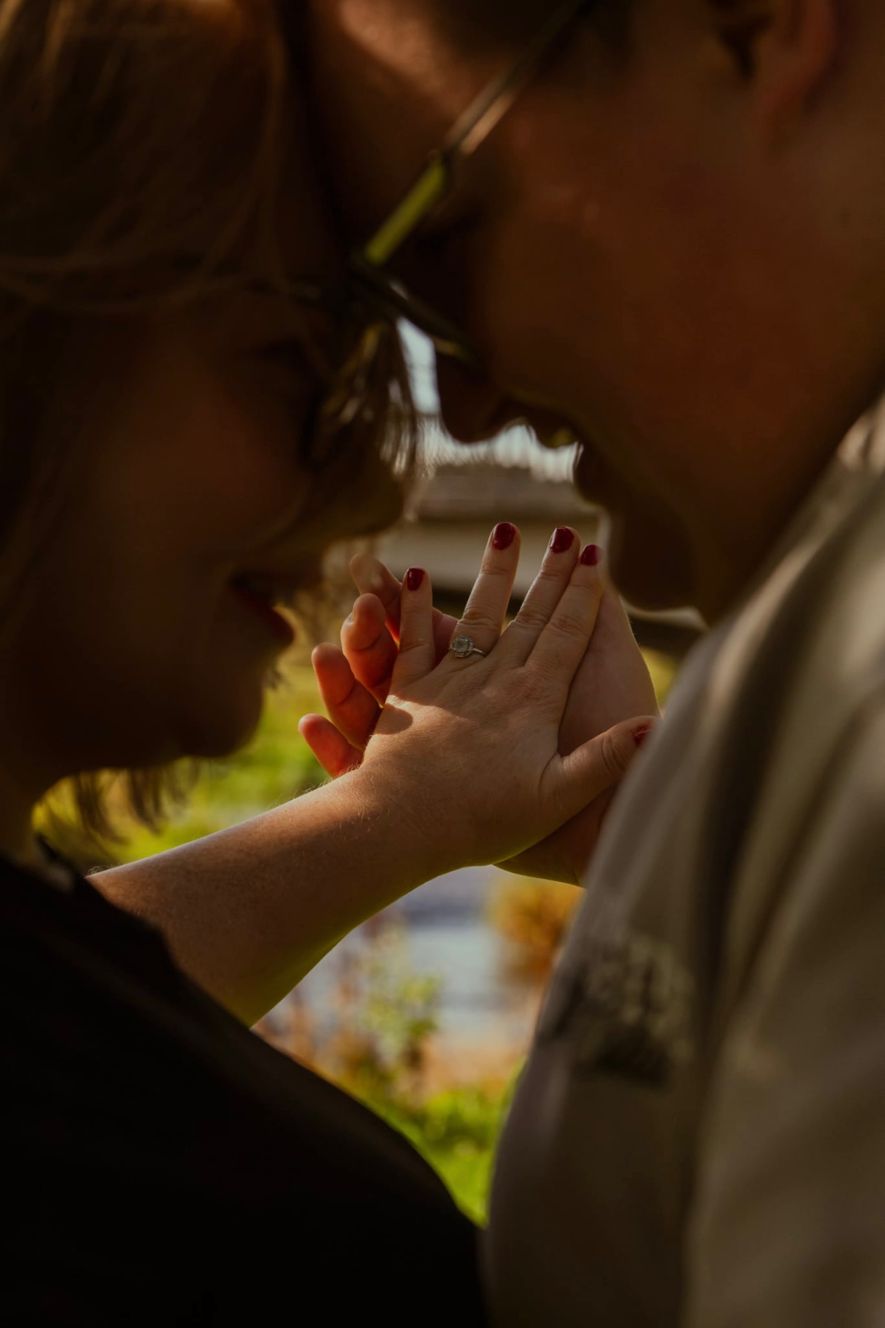 Engagement ring held between two hands in moody purple light